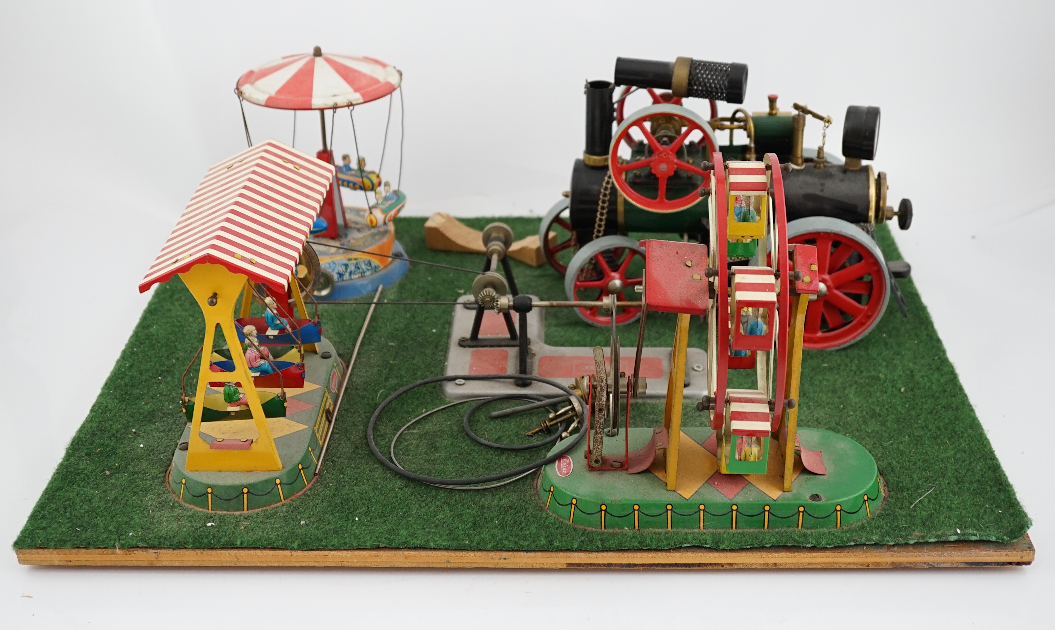 A Wilesco live steam fairground diorama, comprising a D430 pellet fired traction engine, powering a pulley and gear assembly, in turn running three tinplate fairground rides, mounted on a plywood sheet topped with grass